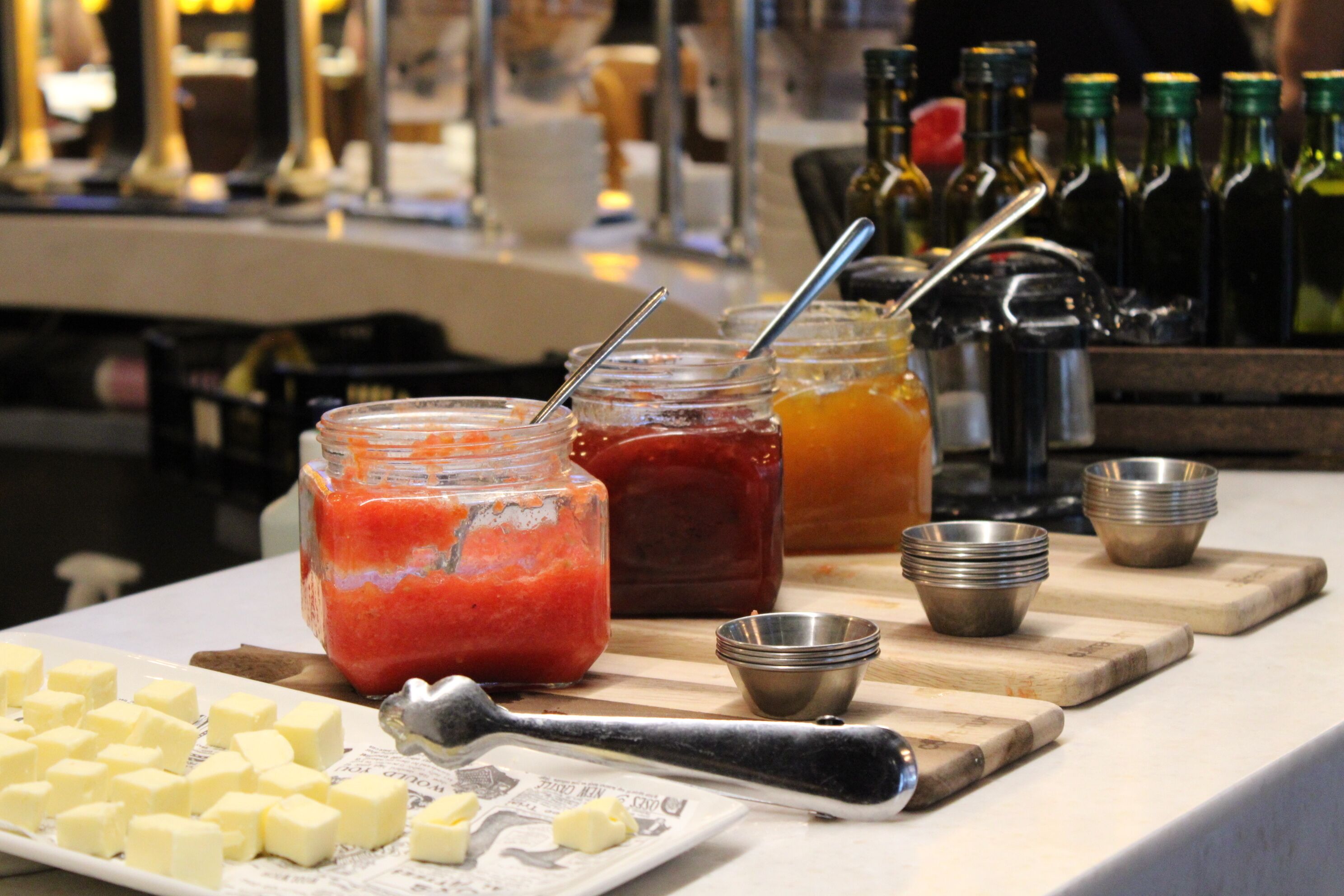 Une table avec des pots de confiture, une planche à découper et une assiette contenant des morceaux de beurre.