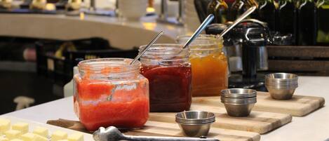 A table with jars of jam, a cutting board, and a plate of butter cubes.