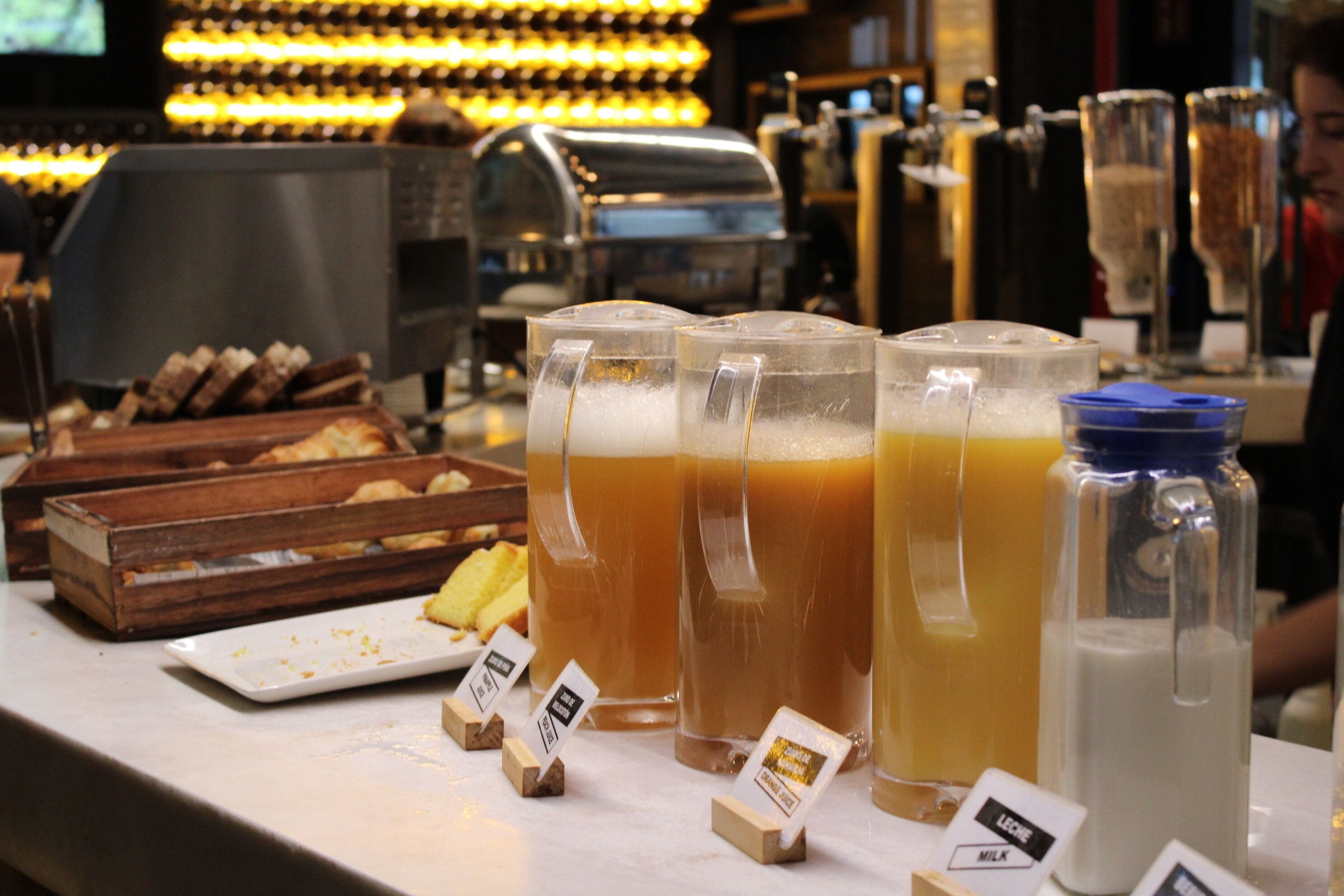 A bar counter with several glasses of beer and a bottle of milk. There are also small wooden blocks with labels.