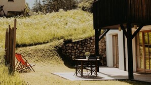 A rustic wooden building with a balcony, a stone wall, and a table with chairs outside.