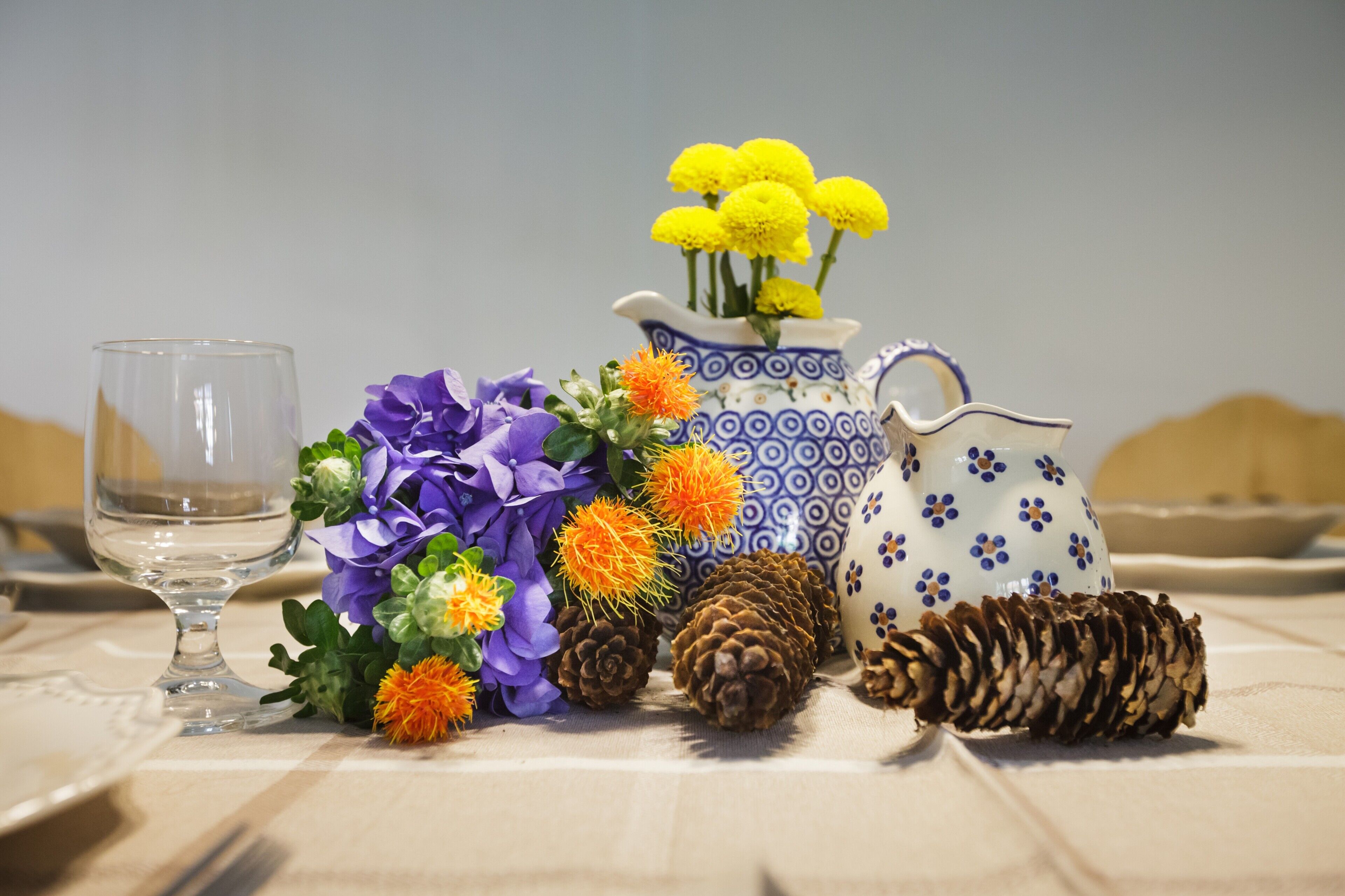 A table setting with a clear glass, a blue and white patterned pitcher, and a variety of flowers.