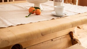 A dining table with a white tablecloth, a bowl of oranges, a chocolate container, and a white cup.