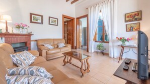 A living room with a sofa, a coffee table, a fireplace, a television, and a window with curtains. - Villa on the Beach with Sea View in Port de Soller. Garden and Wi-Fi (Sóller)