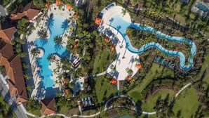 Vue aérienne d’un complexe hôtelier doté d’une grande piscine centrale, de plusieurs petites piscines et d’un toboggan aquatique sinueux.