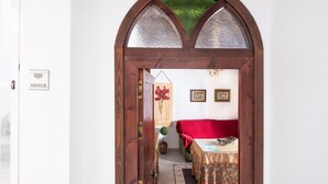 Un arco d'ingresso conduce a una stanza con un letto, un tavolo e una pianta in vaso.