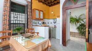 Zona pranzo con tavolo apparecchiato per due, cucina sullo sfondo e una porta che dà su un balcone con piante.