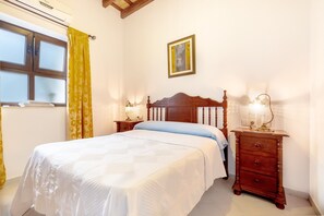 A bedroom with a bed, bedside tables, a window with curtains, a wall-mounted picture, and an air conditioning unit.