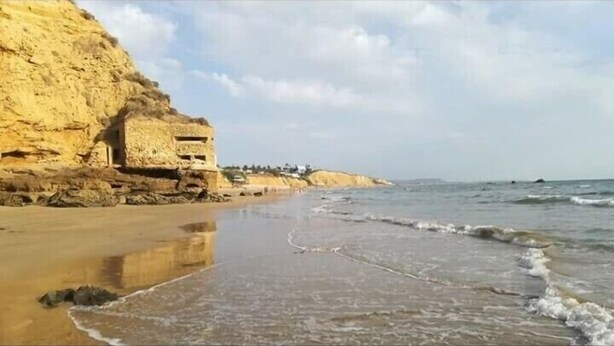 Una spiaggia costiera con una scogliera e un edificio.
