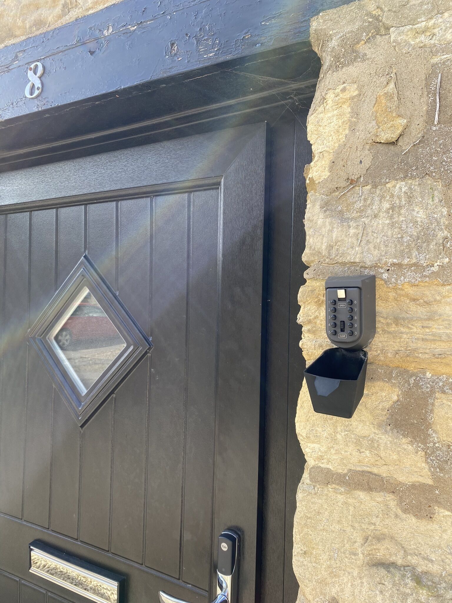 A dark wooden door with a diamond-shaped window and a doorbell button mounted on a stone wall.