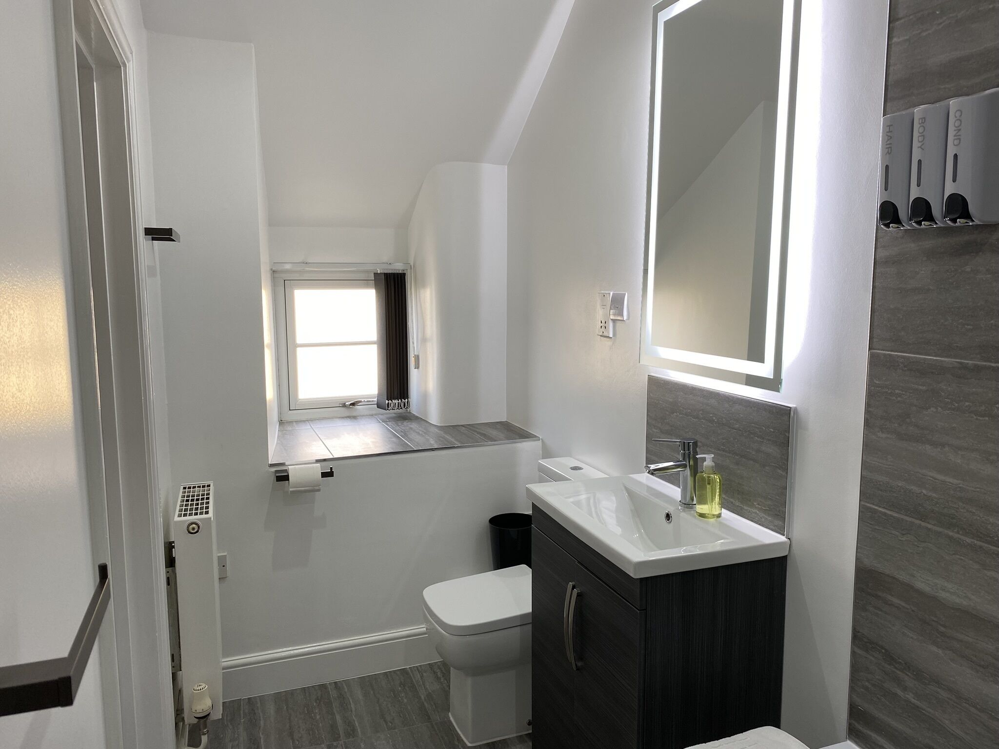 Un baño moderno con ventana, lavamanos e inodoro.