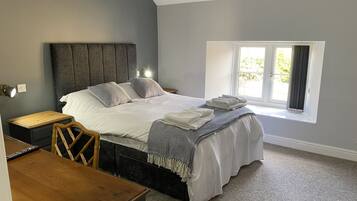 Ein Schlafzimmer mit einem Bett, einem Nachttisch, einem Holzsessel, einem Schreibtisch und einem Fenster mit Vorhängen.