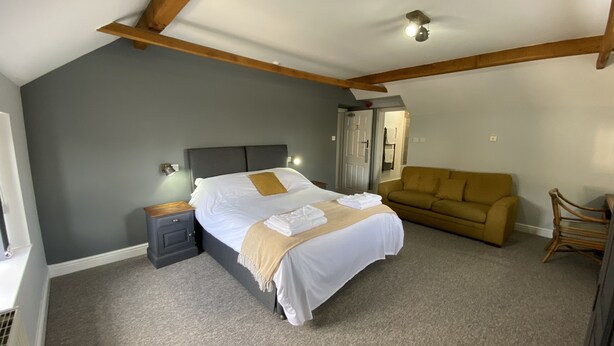 A bedroom with a bed, a nightstand, a sofa, and a chair. - The Roade House Rooms (Northampton)