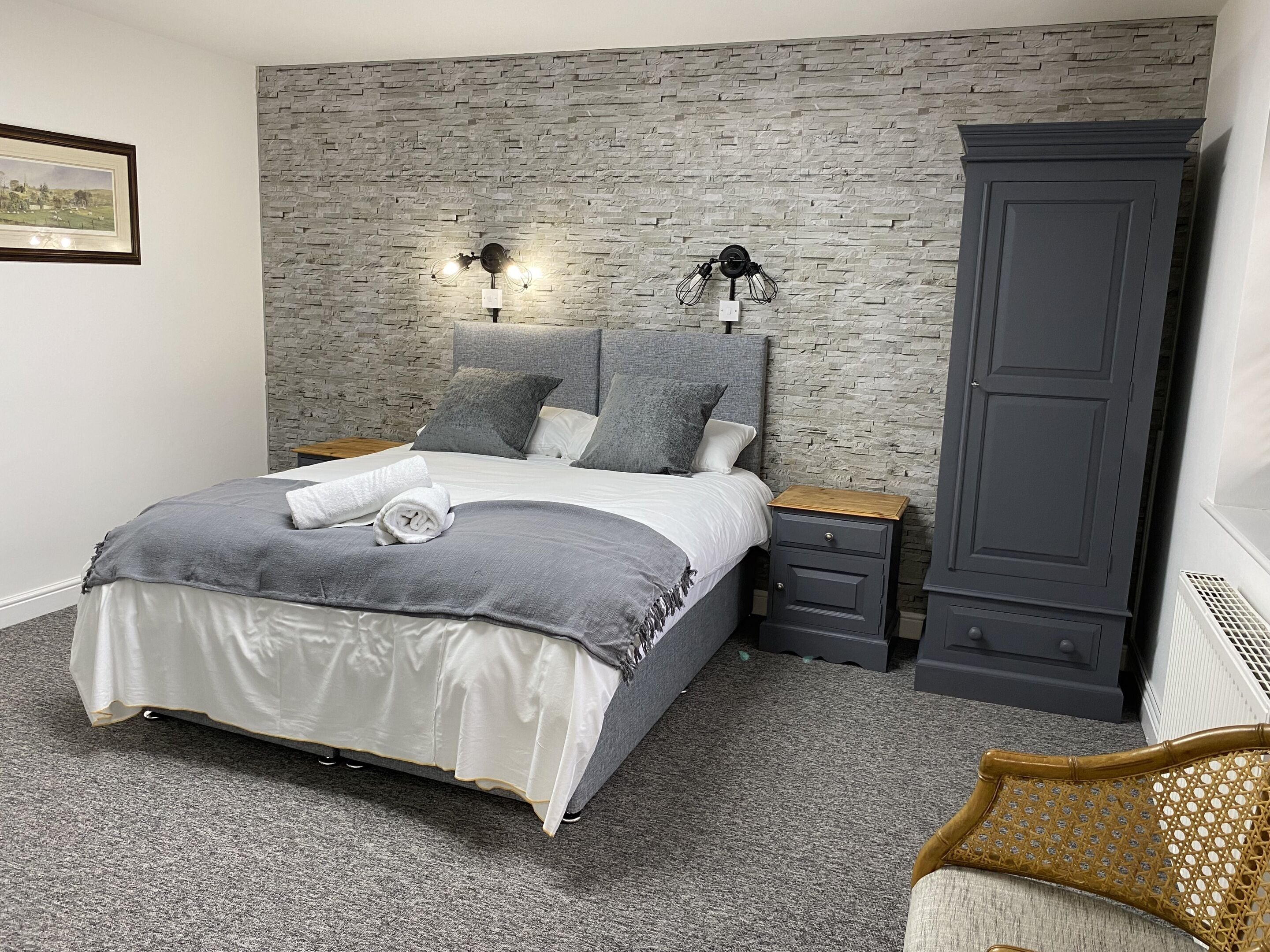 Un dormitorio con cama, ropa de cama gris, un armario gris y un aplique en la pared.