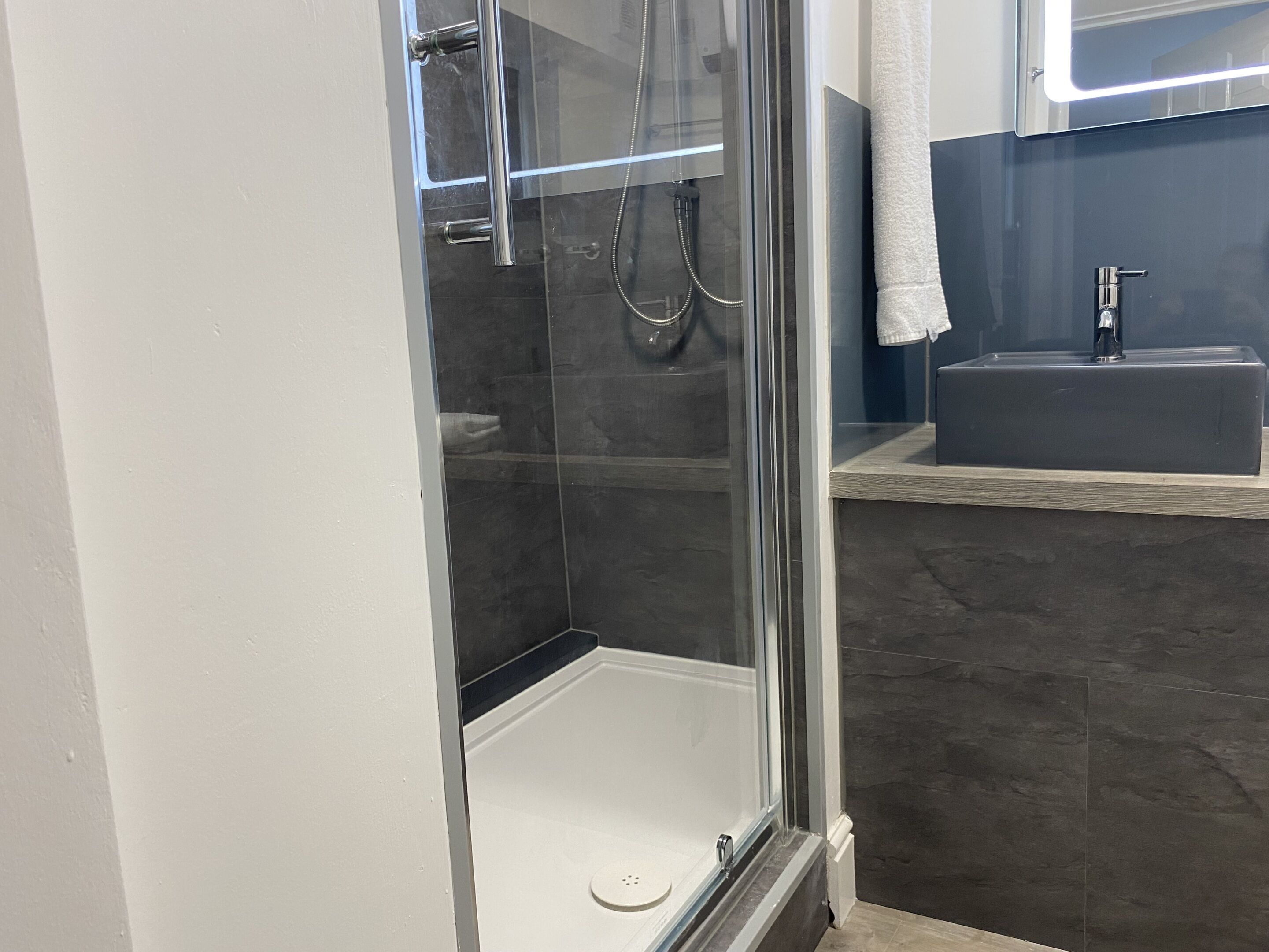 Un baño moderno con ducha envuelta en vidrio, un lavamanos y una toalla colgada en la pared.