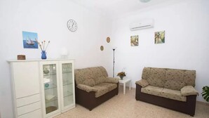 Uma sala de estar com dois sofás, um armário, um relógio e ar condicionado fixado na parede.