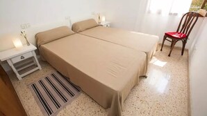 Quarto com duas camas, uma mesa de cabeceira, uma cadeira e uma janela com cortinas.