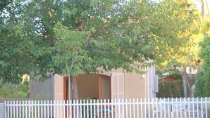 Uma casa com cerca branca, uma árvore na frente e a porta aberta para o exterior.