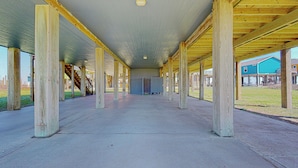 Une galerie intérieure couverte, dotée de colonnes en bois, d’un sol en béton et offrant une vue sur des maisons au loin.