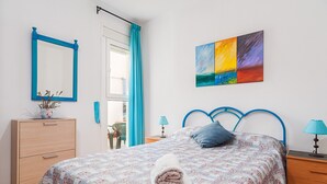 A bedroom with a bed, a dresser, a nightstand, a lamp, a painting, and a window with curtains. - Charming Holiday Apartment with Terrace (Barbate)