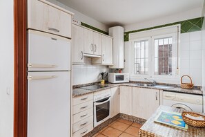 A kitchen with white cabinets, a microwave, an oven, a sink, and a window with bars.