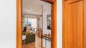 A room with a wooden door, a tiled floor, a green sofa, a dining table with chairs, and a view through a window. - Charming Holiday Apartment with Terrace (Barbate)