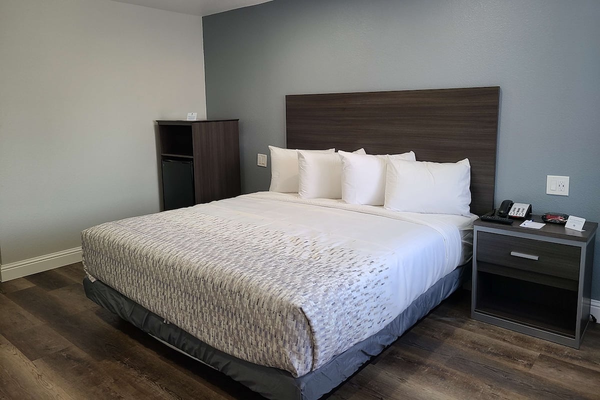 A hotel room with a large bed, a nightstand with a phone, and a small cabinet.