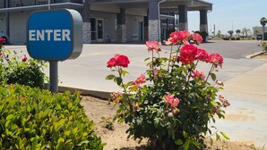 Un edificio con un letrero que dice 'ENTER', un área de estacionamiento techada y un rosal al frente.