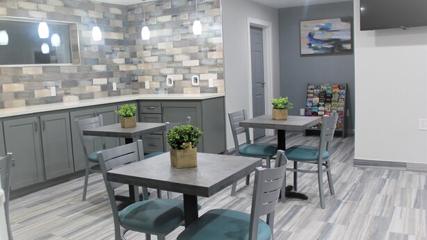 Una cocina moderna con armarios grises, salpicadero de azulejos e iluminación colgante. Hay dos mesas de comedor con sillas, cada una con una planta en maceta.