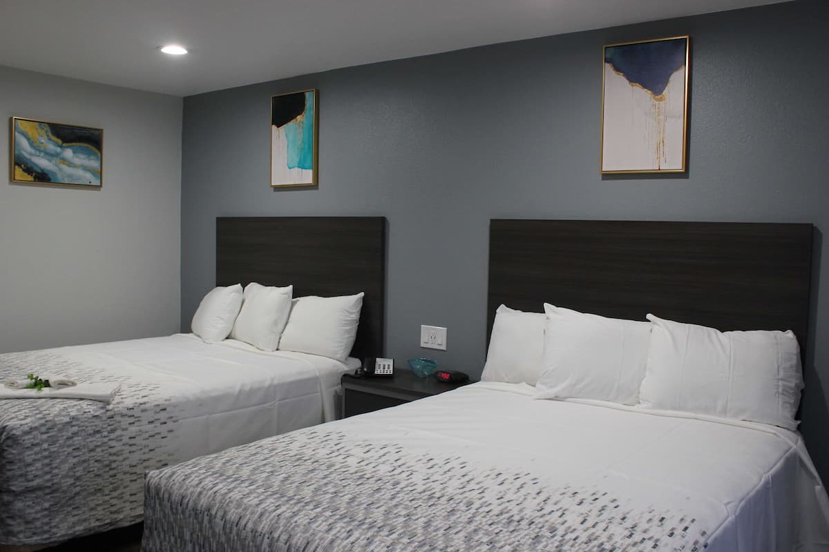 A hotel room with two beds, a nightstand, and artwork on the walls.