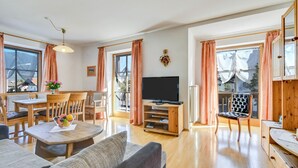 A spacious living area with a wooden dining table, a television on a wooden stand, and a balcony with a view. - Katharinenhof Holiday Apartment "Kramer Sehr Groß" with Balcony, Mountain View & Wi-Fi (Garmisch-Partenkirchen)