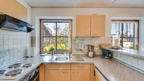 A kitchen with a stove, sink, cabinets, and a window with a view of trees. - Katharinenhof Holiday Apartment "Kramer Sehr Groß" with Balcony, Mountain View & Wi-Fi (Garmisch-Partenkirchen)