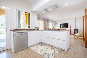 A modern kitchen with white cabinetry, a dishwasher, a large island, and a flat-screen TV mounted on the wall.