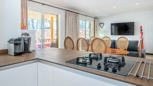 A modern kitchen with a gas stove, a coffee machine, and a dining area with wicker chairs and a table.