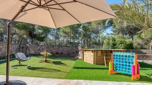 A patio area with a stone floor, a hanging chair, a wooden playhouse, and a pegboard game.