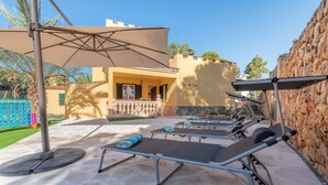 Outdoor sun loungers with umbrellas, a stone wall, and a building with a balcony.
