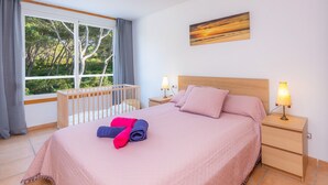 A bedroom with a large window, a crib, a bed with pink bedding, two bedside lamps, and a painting on the wall. - Near the Beach and with Terrace - Can Bennasar (Can Picafort)