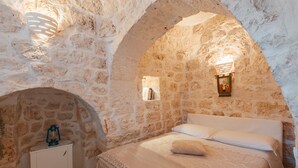 A stone-walled room with a bed, a nightstand, and a wall-mounted light fixture. - Traditional Holiday Home Trullo Milù with WiFi, Air Conditioning (San Michele Salentino)