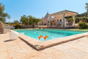 Une piscine agrémentée d’une pergola, de chaises longues et d’un bâtiment en pierre en arrière-plan.