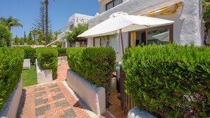 A pathway leading to a building with a white exterior, surrounded by greenery and a palm tree. - Air-Conditioned Vacation Home in Villa Complex with Pool, Beach, Spa, Gym & Wi-Fi (Estepona)