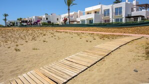 A coastal hotel with a wooden boardwalk leading to white buildings with balconies. - Air-Conditioned Vacation Home in Villa Complex with Pool, Beach, Spa, Gym & Wi-Fi (Estepona)