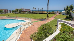 A swimming pool with a surrounding deck, palm trees, and a view of the ocean. - Air-Conditioned Vacation Home in Villa Complex with Pool, Beach, Spa, Gym & Wi-Fi (Estepona)
