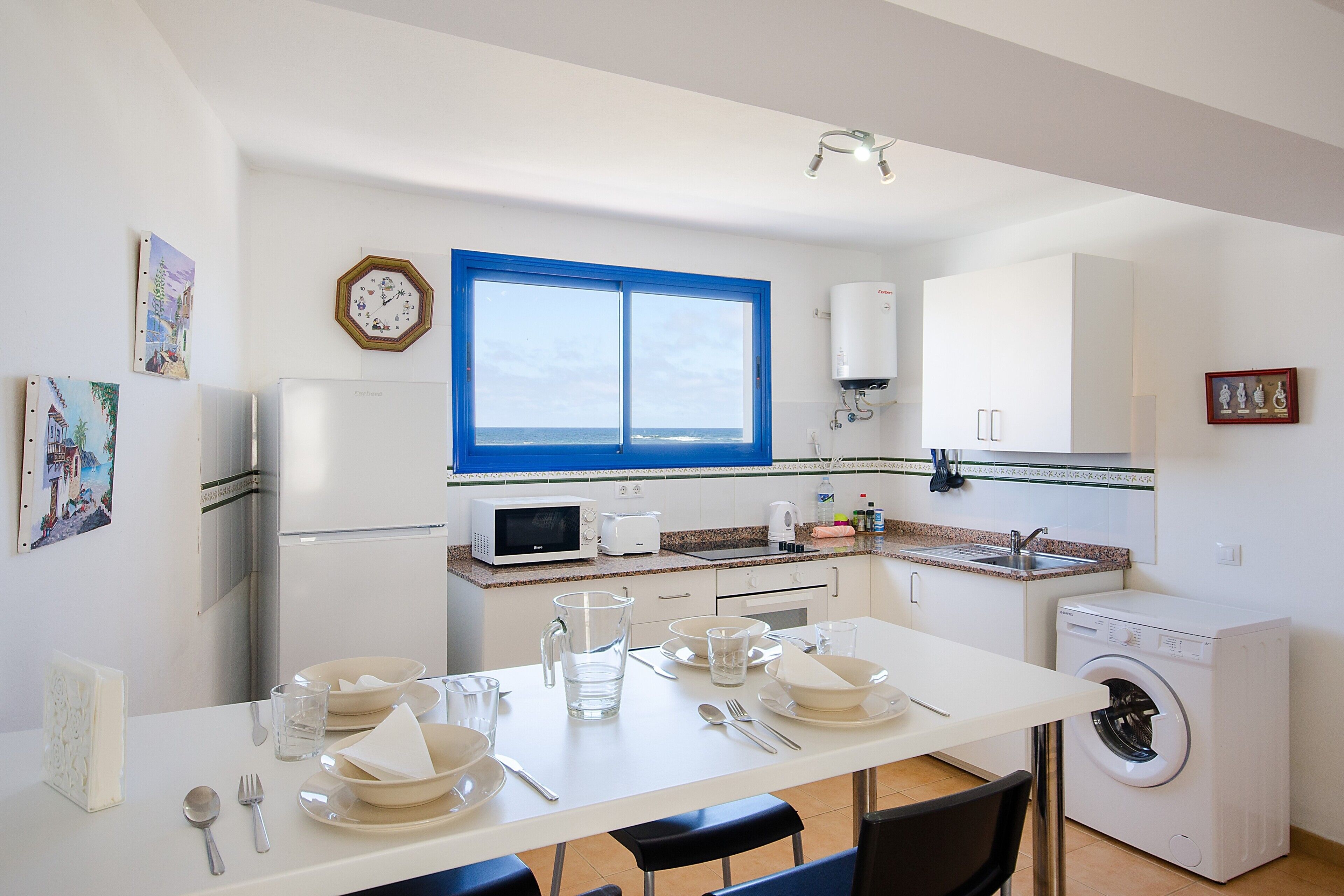 A compact kitchen with a microwave, toaster, sink, and a washing machine.
