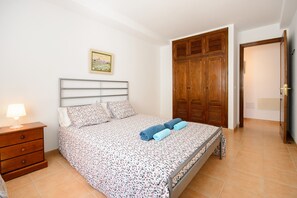 A bedroom with a bed, a nightstand, a wooden wardrobe, and a painting on the wall. - Charming Seafront Apartment with Balcony and Wi-Fi (Orzola)