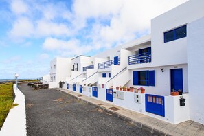 A row of white buildings with blue doors and windows, a gravel path, and a clear sky.