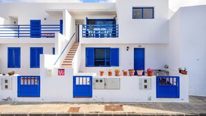 Un bâtiment blanc avec des portes et des volets bleus, un escalier et des plantes en pot.