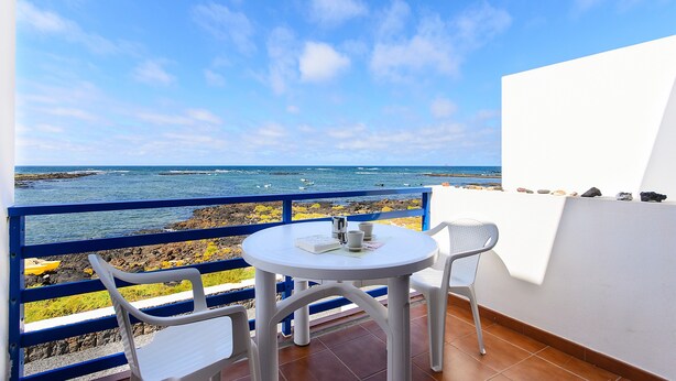 Un balcon avec une table et des chaises blanches, donnant sur une côte rocheuse et la mer.