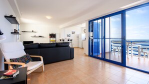 Un salon moderne comprenant un canapé, un coin repas et une vue sur la mer, visible à travers une porte vitrée.