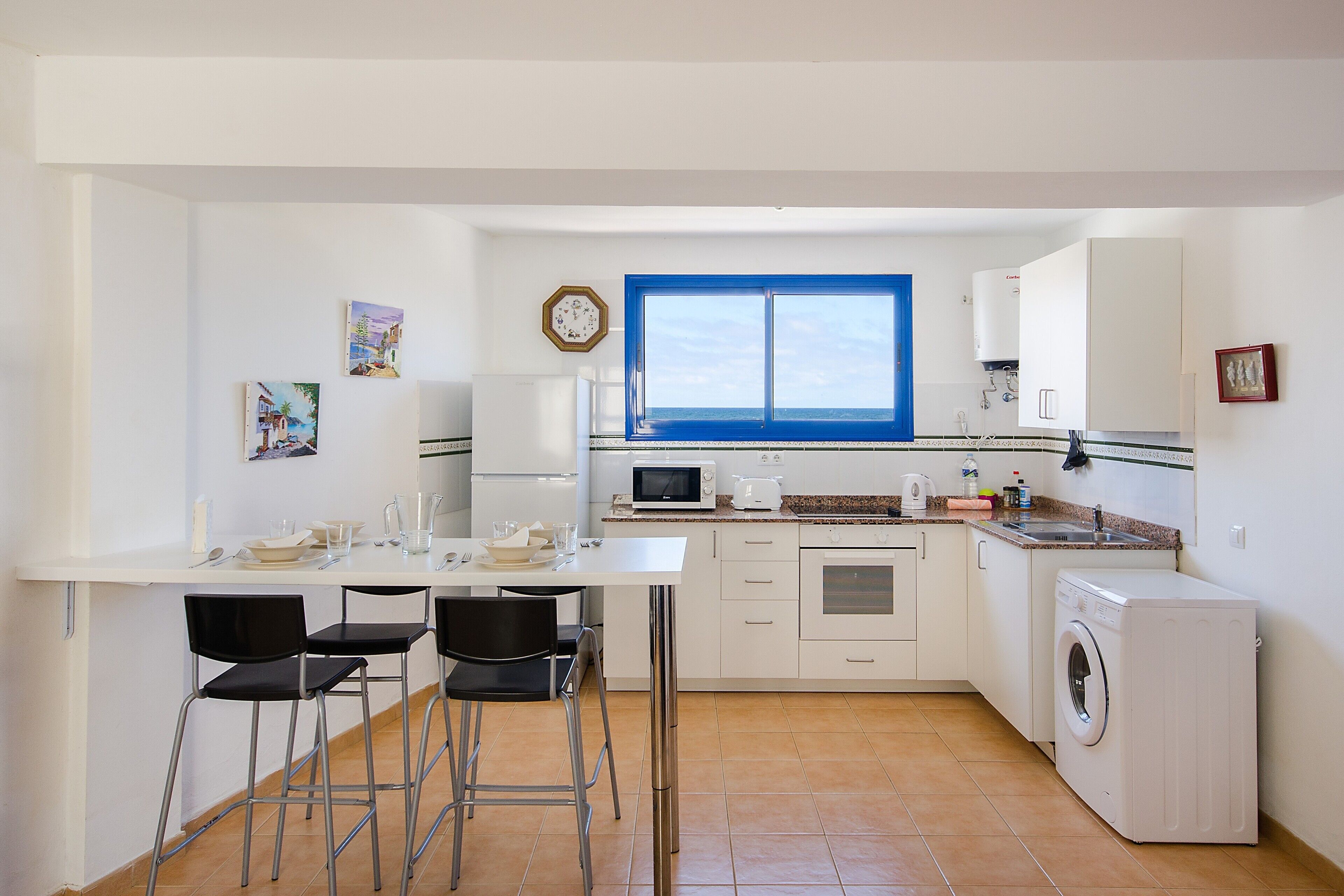 Cocina compacta con comedor, lavadora y un amplio ventanal.