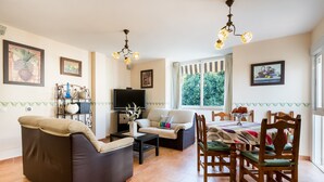 Una sala de estar con sofá, mesa de centro, televisor, mesa de comedor con sillas y obras de arte en las paredes.