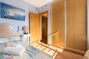 Een slaapkamer met een bed, nachtkastje, lamp, garderobe en een schilderij van een waterval.